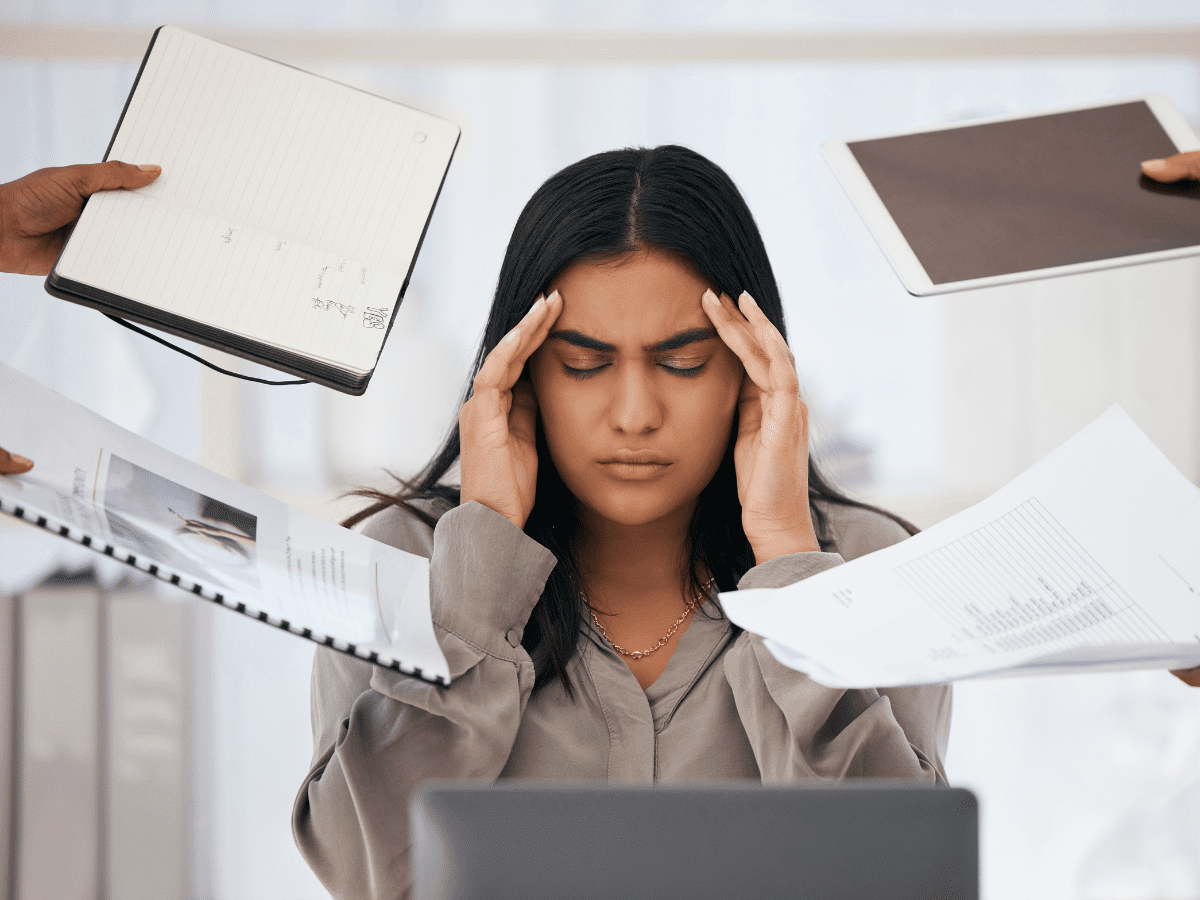 A woman massaging her temples being overwhelmed with paperwork and deadlines