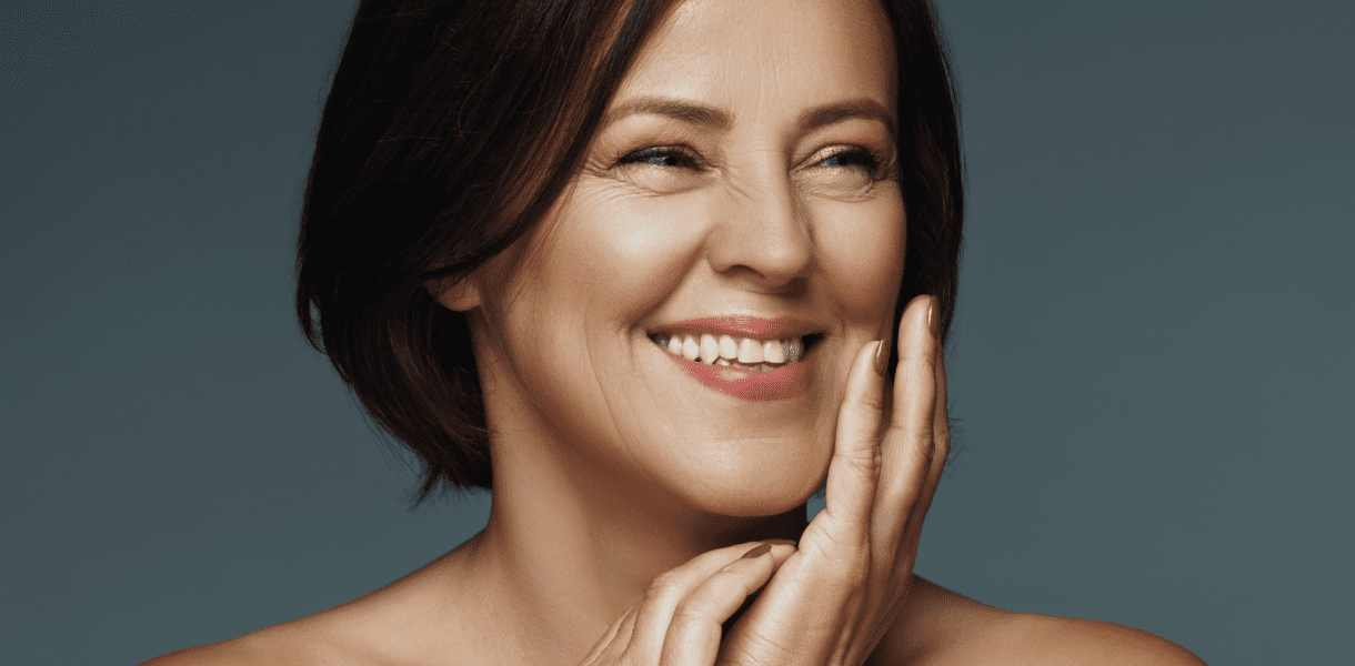 brown-haired woman smiles brightly while touching face
